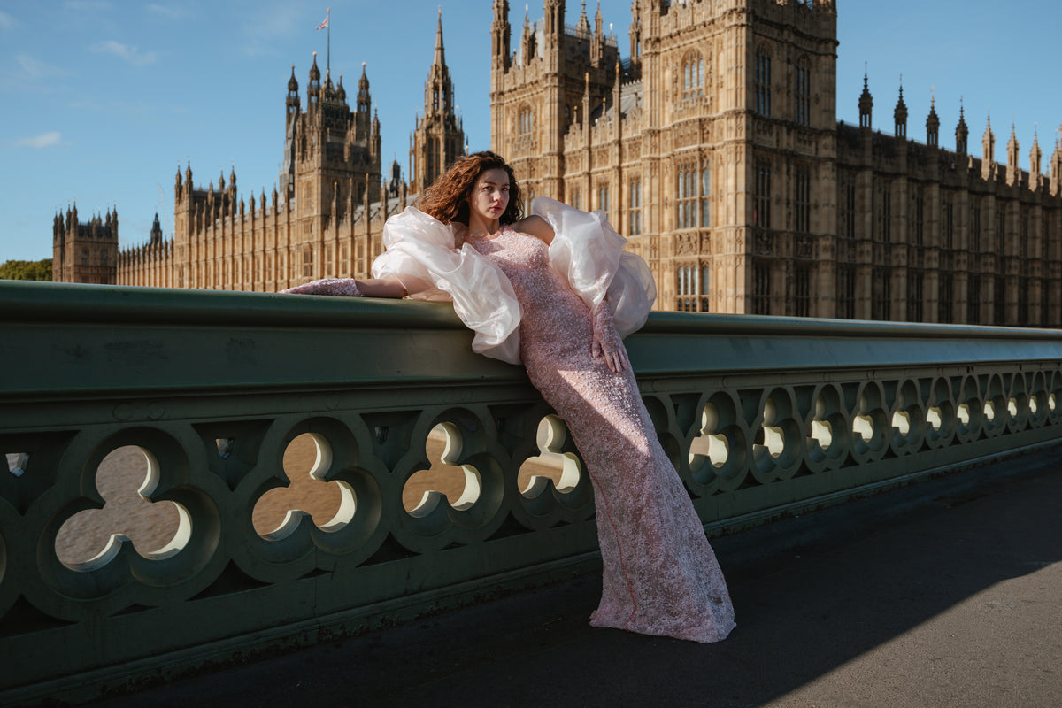 Model wearing a pale pink gown with voluminous white sleeves on Westminster Bridge.